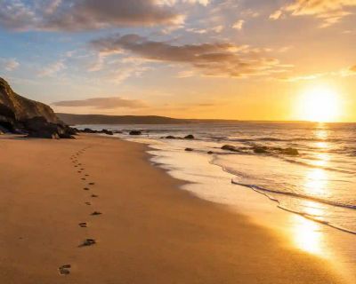 A UK beach at golden hour with footprints leading along the shoreline.